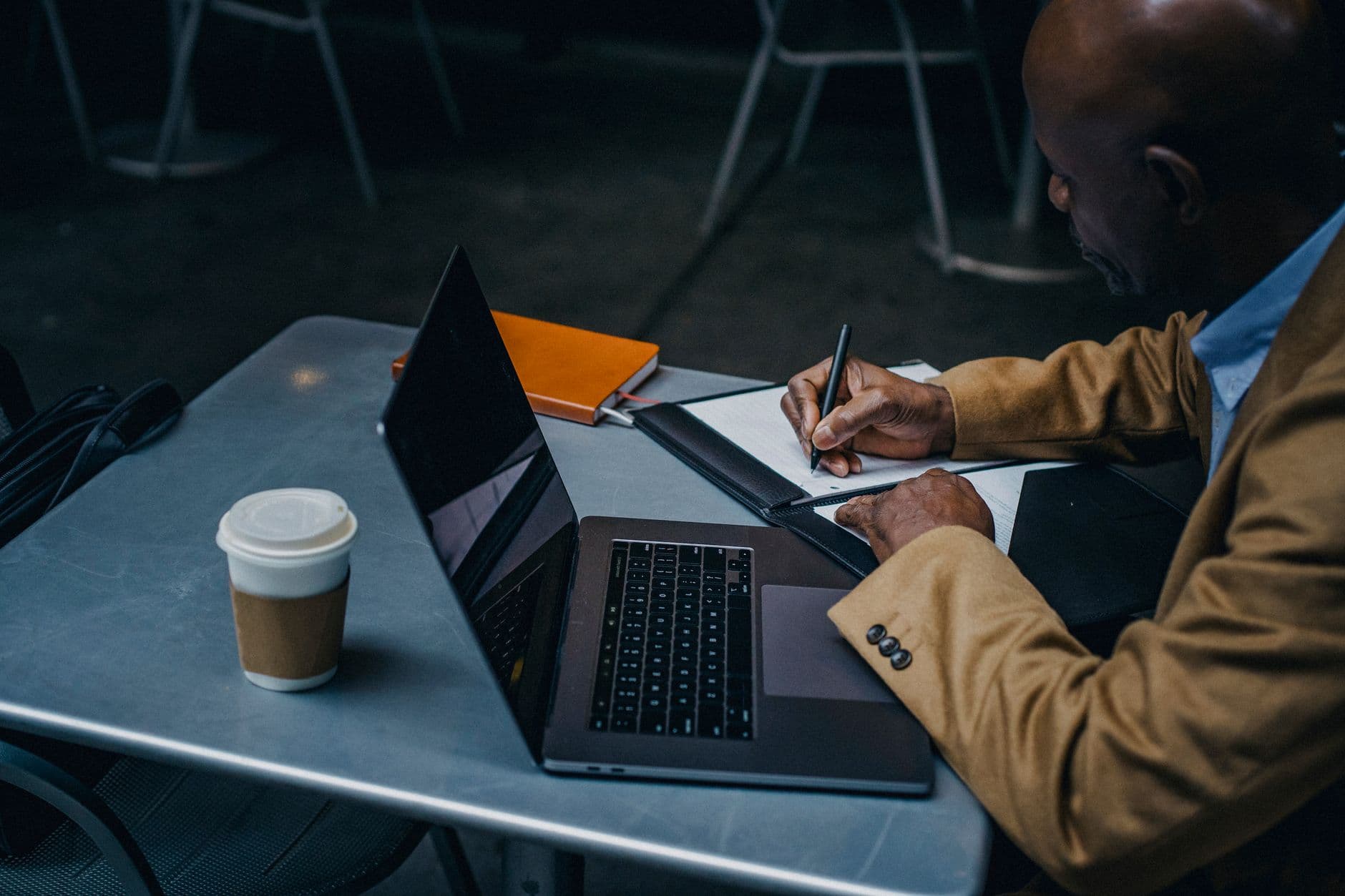 A person writing notes at a laptop in a cafe